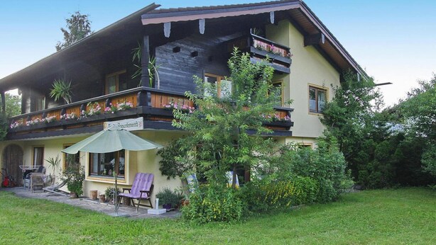 A two-story house with a balcony, a patio with outdoor furniture, and a garden. - Holiday Flat in Schonau am Konigssee (Schoenau am Koenigssee)