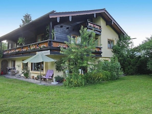 A two-story house with a balcony, a patio with outdoor furniture, and a garden.