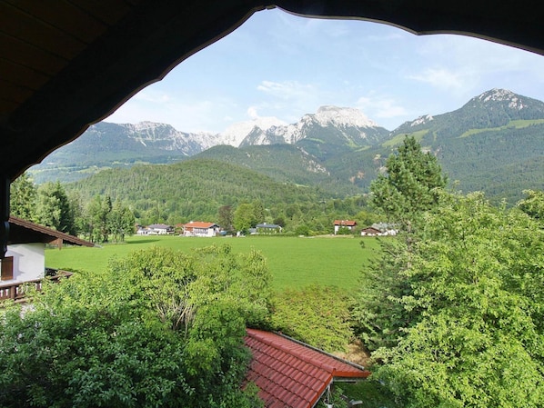 A mountain view from a covered area with a red roof, overlooking a green valley and houses.