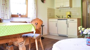 A cozy kitchen with a wooden table, a chair, and a window with curtains. - Holiday Flat in Schonau am Konigssee (Schoenau am Koenigssee)