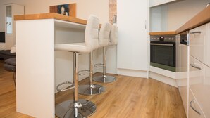 Una cocina moderna con armarios blancos, horno empotrado y dos taburetes de bar con asientos acolchados.
