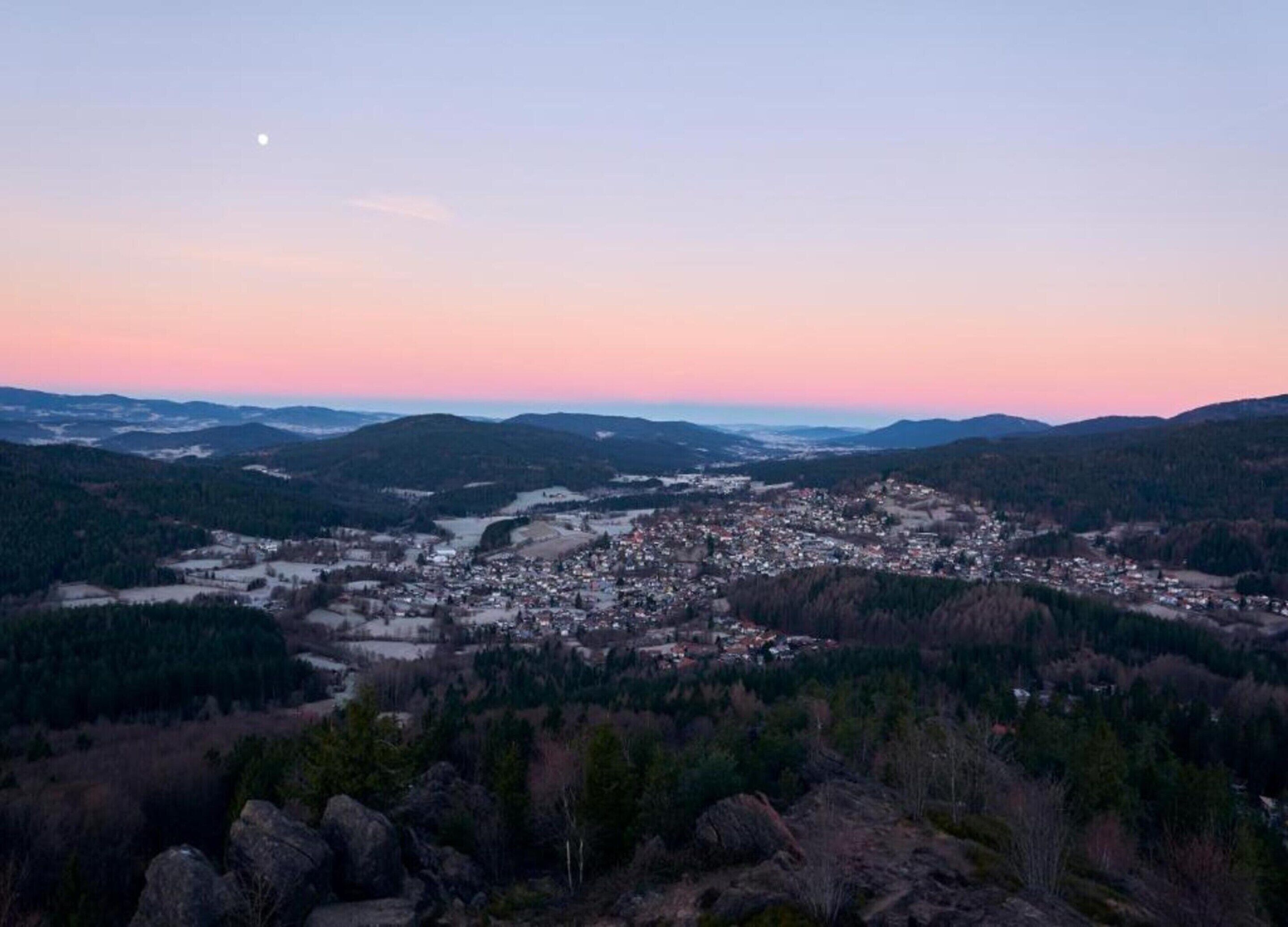 A town nestled in a valley with a river running through it, surrounded by hills and forests.