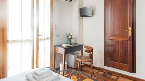 Quarto com cama, escrivaninha com cadeira, televisão na parede e porta de madeira.