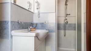 Uma casa de banho com lavatório, dois secadores de cabelo fixados na parede e chuveiro com chuveiro de mão.