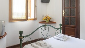 Une chambre à coucher avec un lit, une fenêtre avec des rideaux, une porte en bois et une petite étagère ornée de fleurs.