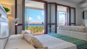 Habitación de hotel con cama, sofá, balcón y vista al mar, además de una lámpara.