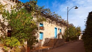 Una estrecha calle con un edificio de fachada de piedra, puertas azules y una escalera que conduce a la entrada.
