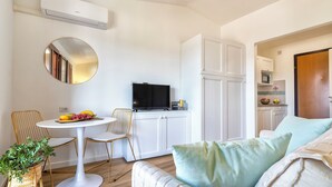 Un espacio habitable compacto con un espejo redondo, una mesa de comedor con sillas, un sofá, un televisor y una kitchenette.