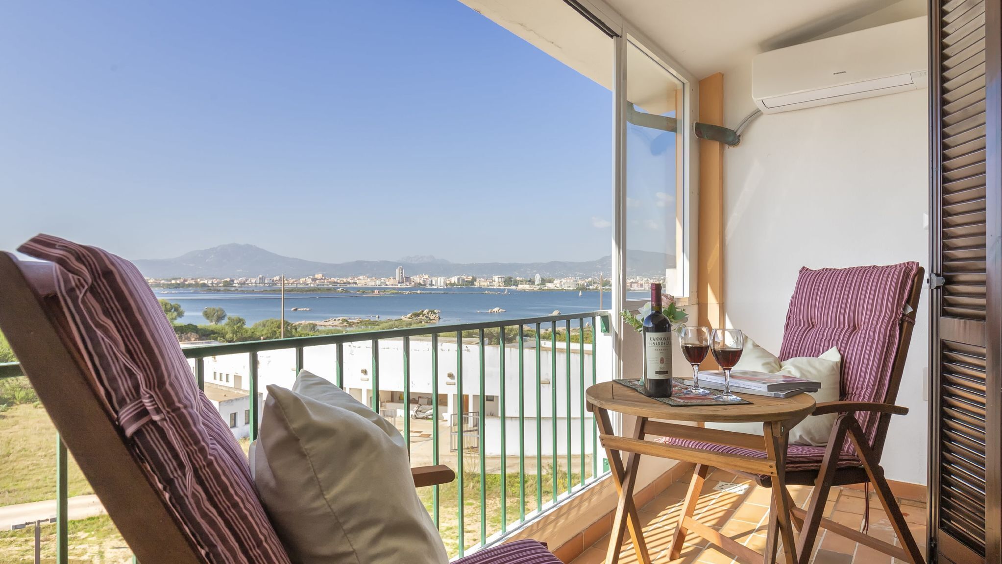 Ein Balkon mit Tisch, zwei Stühlen, einer Weinflasche und einem Glas.