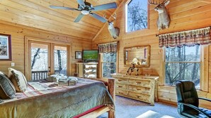 Une chambre aménagée dans un chalet en rondins, avec un lit, un bureau, une chaise, un téléviseur et des bois de cerf accrochés aux murs.