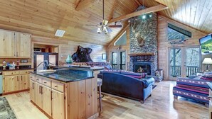 Un interior de cabaña de madera espaciosa, con una isla de cocina grande, chimenea de piedra y una zona de estar acogedora.