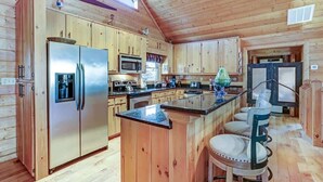 L’intérieur d’un chalet en bois comprend une cuisine équipée d’un réfrigérateur en acier inoxydable, d’un four à micro-ondes et d’une cuisinière. On y trouve également un comptoir-bar en bois avec des tabourets.