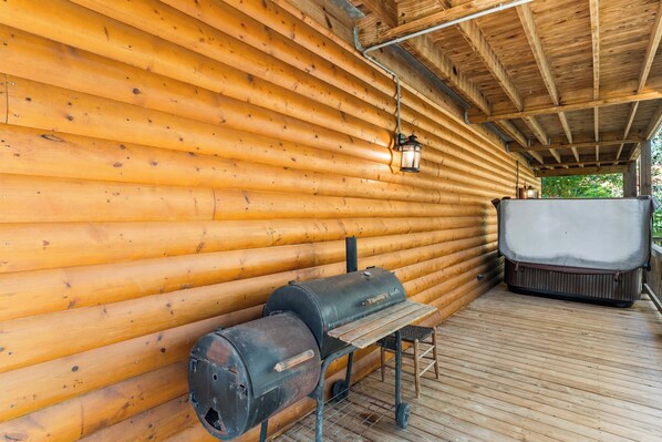 A wooden log cabin with a hot tub, a grill, and a lantern.