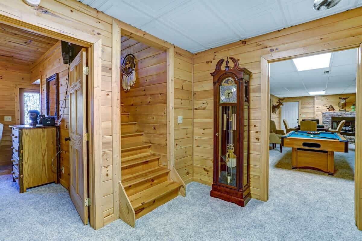 Un interior de madera con una escalera, un reloj y una mesa de billar.