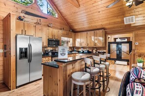 A wooden cabin kitchen with a central island, stainless steel appliances, and a ceiling fan.