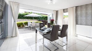 Een moderne keuken met roestvrijstalen apparatuur, een eethoek met een glazen tafel en stoelen, en uitzicht op een tuin door de glazen deur.