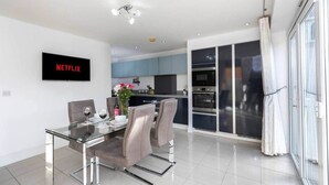 Een moderne keuken met een eethoek, een televisie waarop 'NETFLIX' wordt weergegeven, en een grote schuifpui.