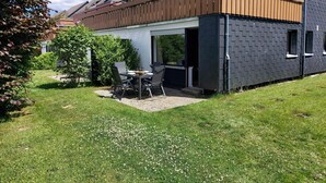 A modern house with a patio area featuring a table and chairs, surrounded by a well-maintained lawn and trees. - Moderne Wohnung in Winterberg Nahe Skigebiet (Winterberg)