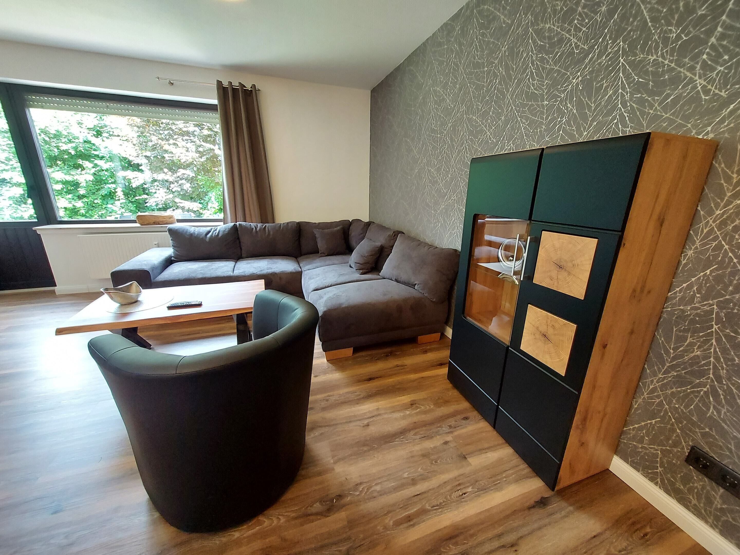 A modern living room with a sectional sofa, a black armchair, a wooden coffee table, and a built-in cabinet with a unique design.