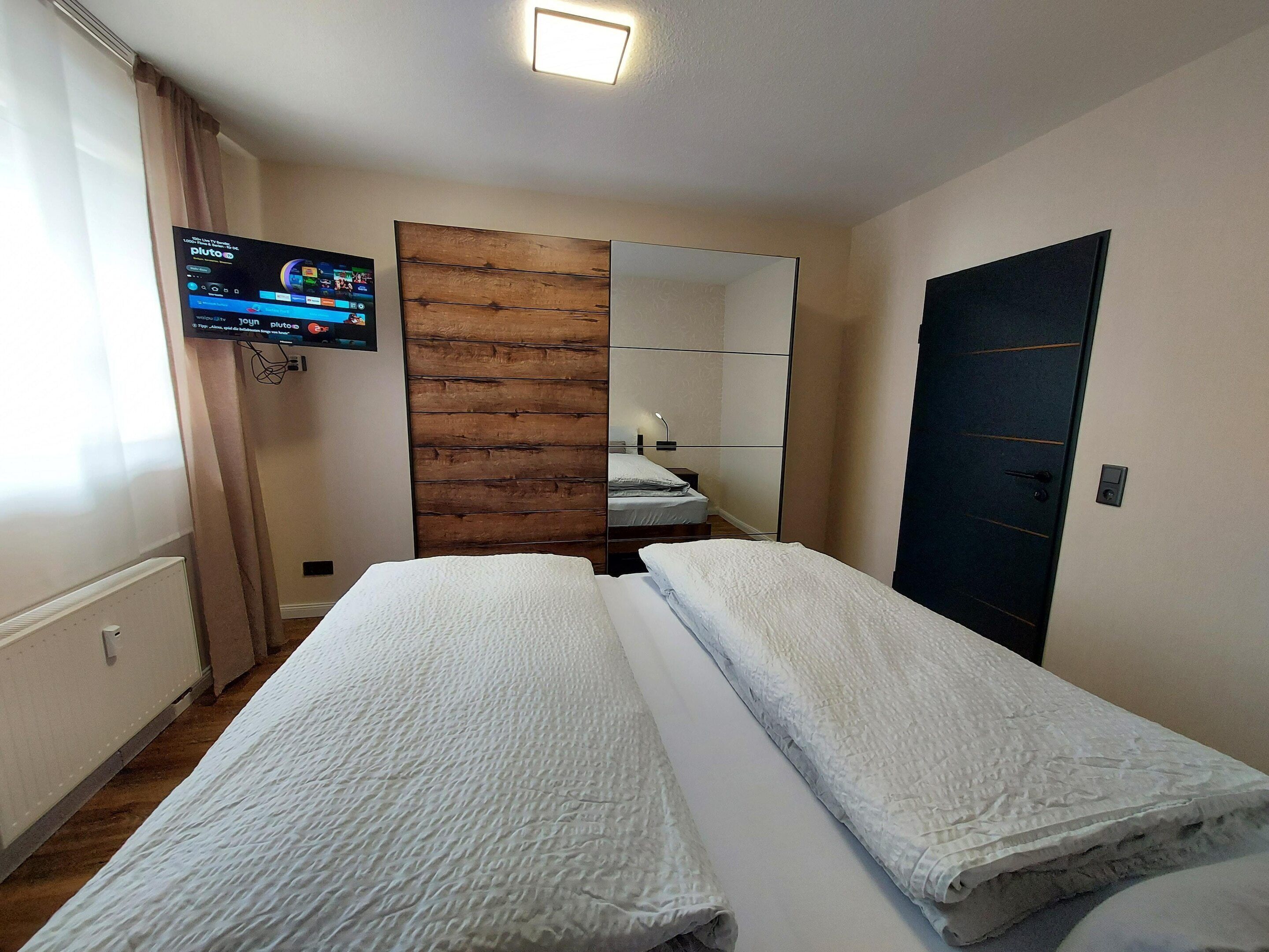 Hotelkamer met twee bedden, een aan de muur bevestigde televisie, houten paneelbekleding, een deur en een lamp.