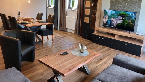 A modern living room with a dining area, wooden furniture, a flat-screen TV, and a plant. - Moderne Wohnung in Winterberg Nahe Skigebiet (Winterberg)