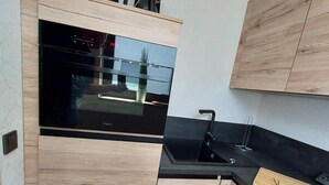 A modern kitchen with wooden cabinetry, a black sink, and a built-in Amica TV. - Moderne Wohnung in Winterberg Nahe Skigebiet (Winterberg)