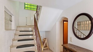 Un escalier aux marches beiges et aux contremarches sombres, menant à un palier où se trouvent un banc en bois et un miroir accroché au mur.