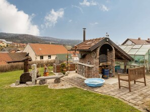 A rustic outdoor kitchen with a brick oven, a wooden bench, and a small pool. - Apartment in Gleissenberg With Garden & BBQ (Gleissenberg)