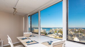 A balcony with a table and chairs, overlooking a coastal town. - Beautiful sunset and ocean view from 2 Bedroom Condo with Free WiFi and an Outdoor Pool Located in Midtown Only Steps to Beach! (Ocean City)