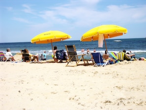 A beach with people relaxing under yellow umbrellas, some in beach chairs, and the ocean in the background.