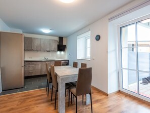A modern kitchen with a dining table and chairs, a built-in oven, and a window with a view. - Garden Apartment in Haunsheim (Haunsheim)