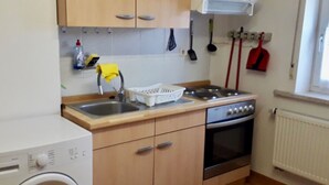 Een kleine keuken met houten kastjes, een ingebouwde oven, een wasmachine en een raam met een radiator.