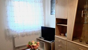 Een kamer met een houten tafel, een vaas met bloemen, een televisie en een kast.