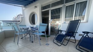 A covered outdoor area with a table and chairs, a large window, and a door leading inside. - Apartments LAS CARACOLAS, Puerto de Mogán 1C (Puerto de Mogán)