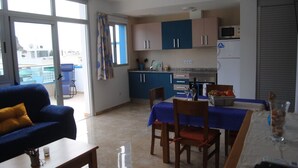 A modern kitchen with blue cabinets, a dining table set with chairs, and a sofa in the living area. - Apartments LAS CARACOLAS, Puerto de Mogán 1C (Puerto de Mogán)