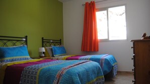 A room with two beds, a window with orange curtains, a wooden dresser, and a green wall. - Apartments LAS CARACOLAS, Puerto de Mogán 1C (Puerto de Mogán)