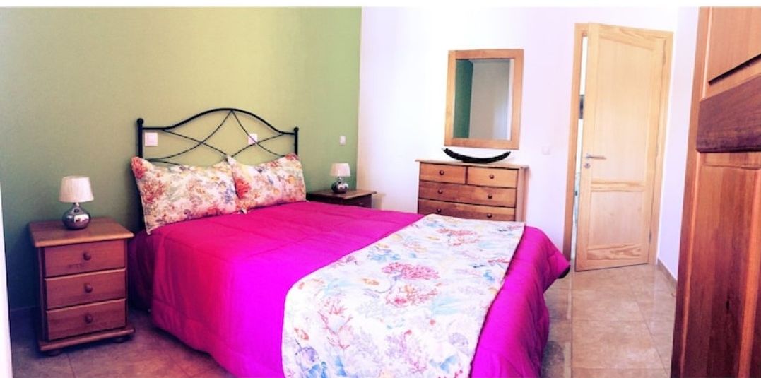 A bedroom with a bed, a nightstand, a dresser, a mirror, and a door.