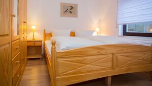 Ein Schlafzimmer mit einem hölzernen Bett, zwei Nachttischen mit Lampen, einem Kleiderschrank und einem Fenster mit Jalousien.
