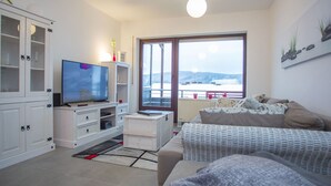 Ein modernes Wohnzimmer mit großem Fernseher, weißen Schränken, einer Couch und einem großen Fenster mit Blick auf eine verschneite Landschaft.