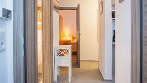 Ein Flur mit einer Holztür, einem kleinen weißen Tisch und einem Bett im Hintergrund.