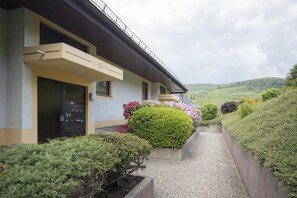 Un bâtiment doté d’un porche, d’un petit balcon et d’un chemin menant à un espace paysager agrémenté d’arbustes et de fleurs.