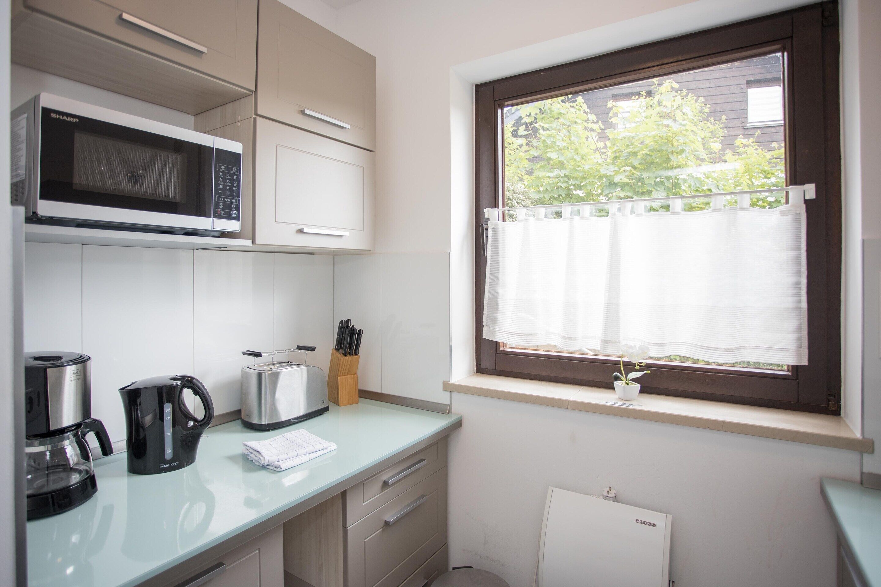Eine kleine Küche mit Mikrowelle, Toaster, Kaffeemaschine und einem Fenster mit Jalousien.