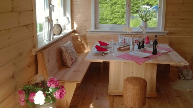 A wooden cabin interior with a wooden bench, a dining table with pink placemats, and a window with a view of greenery. - Forest Escape Near Ski Lift (Medebach)