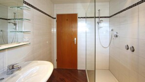 A bathroom with a wooden door, a glass shower enclosure, and a white sink with a mirror above it. - Cosy Flat in Schonau am Konigssee (Schoenau am Koenigssee)