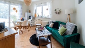 Un salon avec un canapé vert, une table à manger avec des chaises, une table basse et un téléviseur.