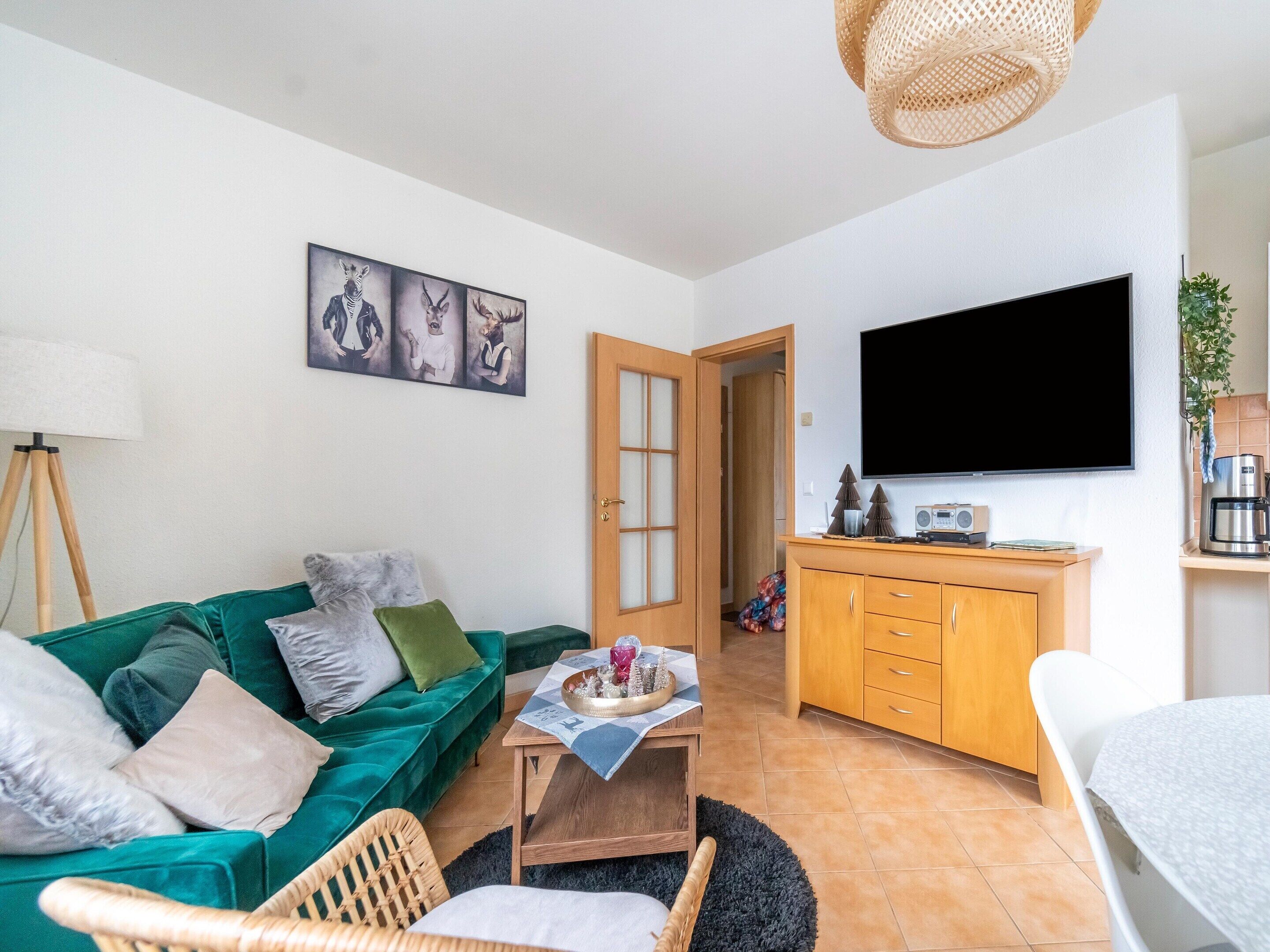 Un salon avec un canapé vert, un meuble en bois, un téléviseur à écran plat et un coin repas comprenant une table et des chaises.