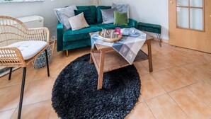 Un salon chaleureux avec un canapé de couleur turquoise, un fauteuil en osier, une table basse en bois et un tapis noir.