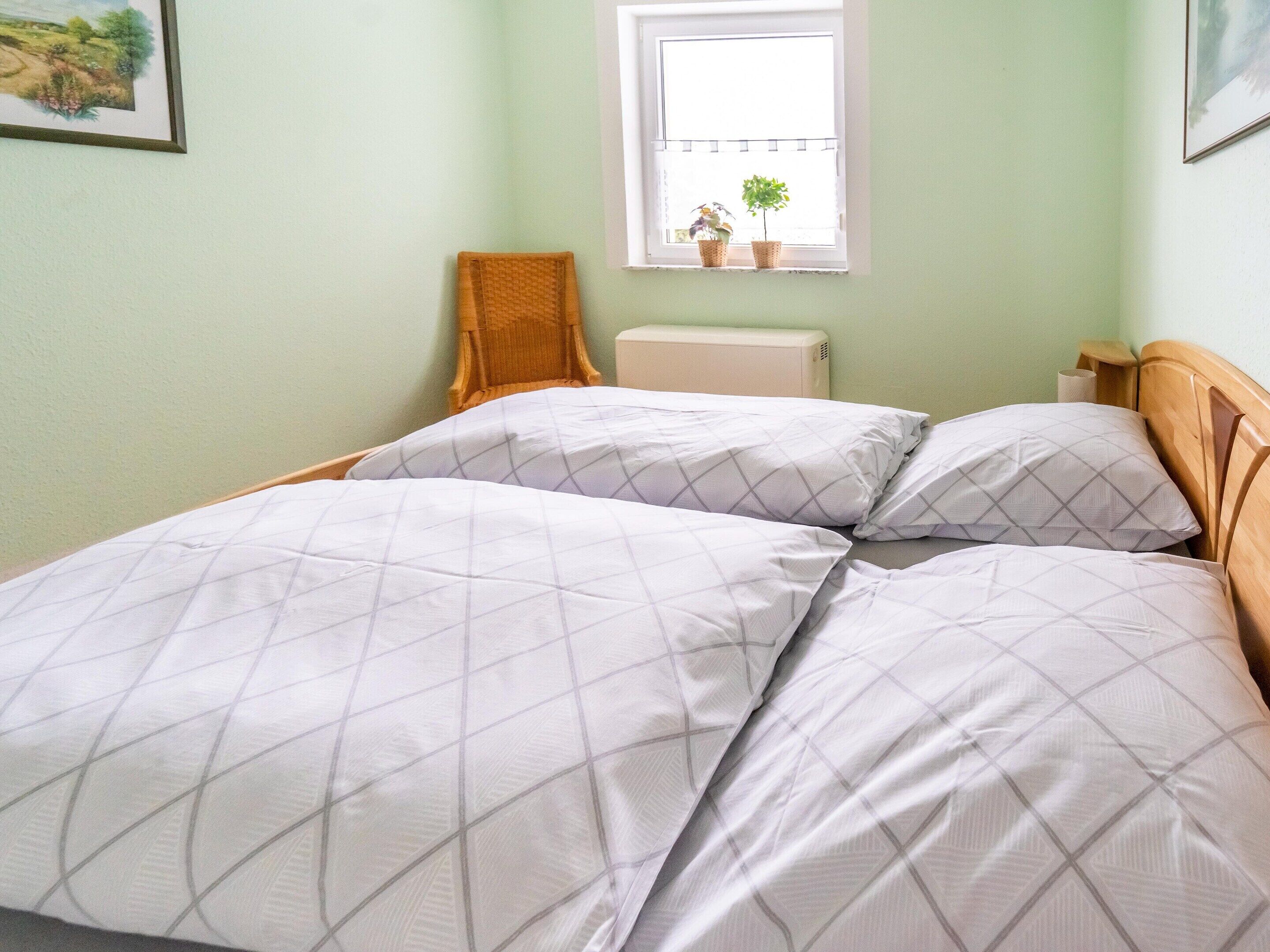 Une chambre à coucher avec un lit, une chaise, une fenêtre avec des plantes et un radiateur.