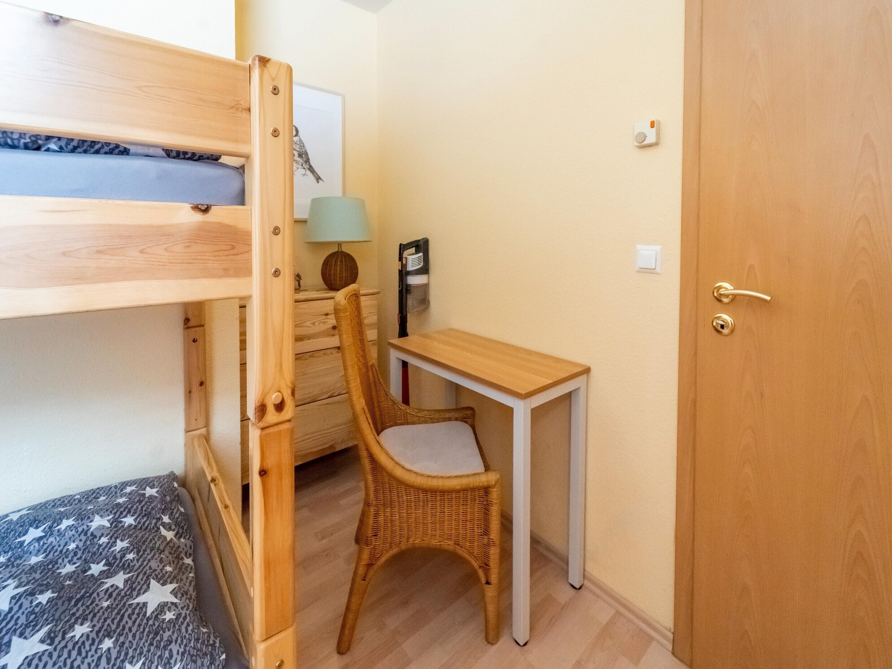 A bunk bed with a star-patterned pillow, a wicker chair, a small wooden desk, a lamp, and a door with a handle.