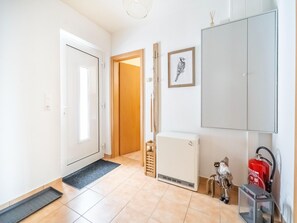 Corredor com uma porta branca, uma porta de madeira, um radiador, um extintor de incêndio e um quadro na parede.